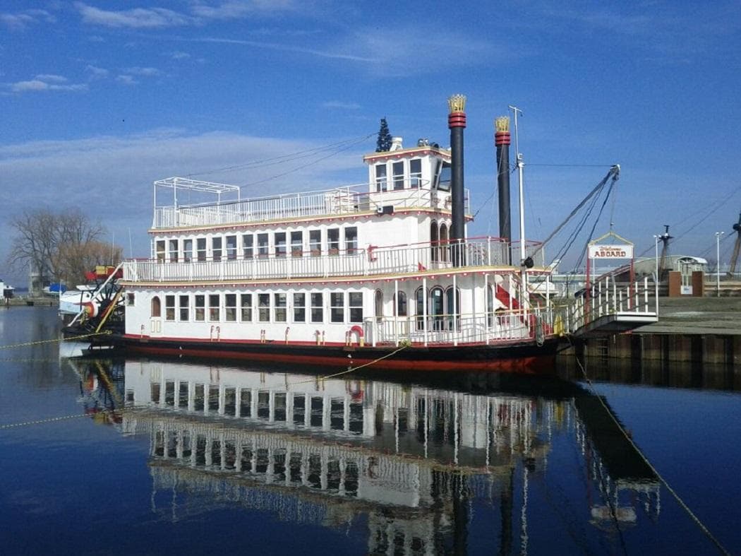 White paddlewheel steamboat reflected on calm river, morning light