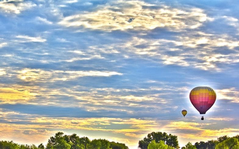 Hot air balloon floating over tree-lined sunrise horizon