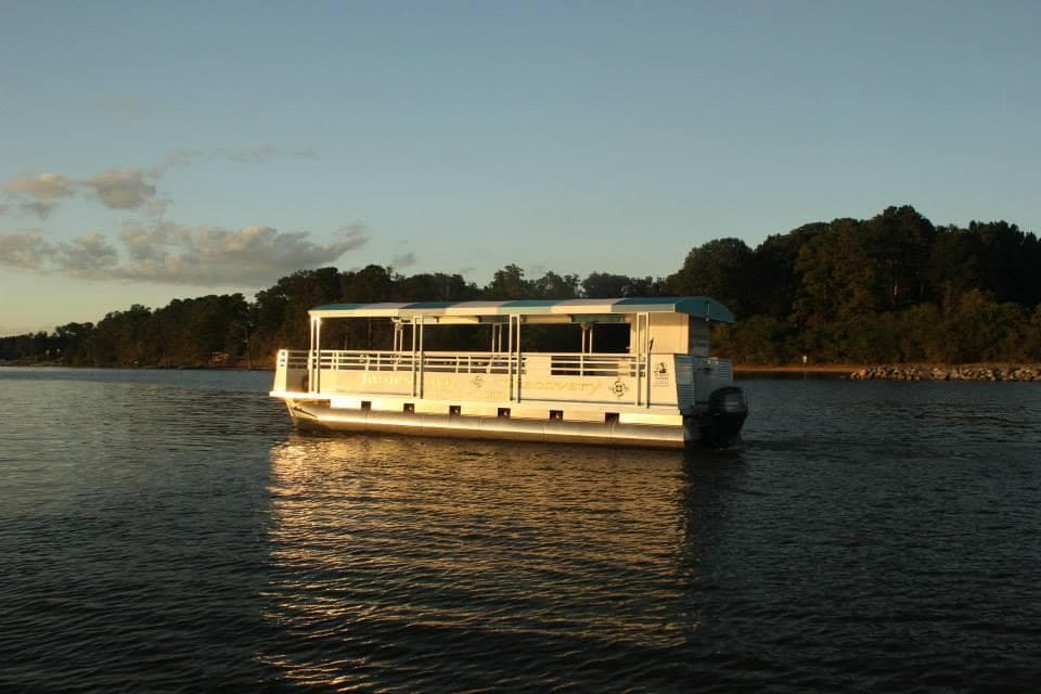 Daytime river cruise boat near wooded shoreline on James River