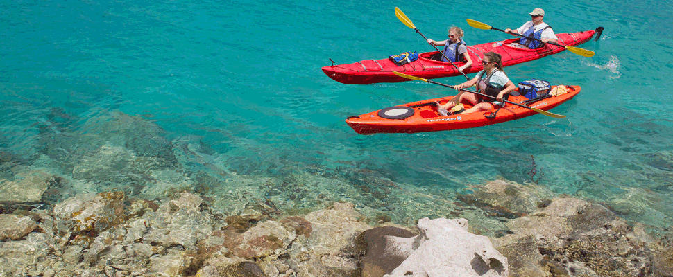 Kayakers paddling clear turquoise coastal water near rocky reef