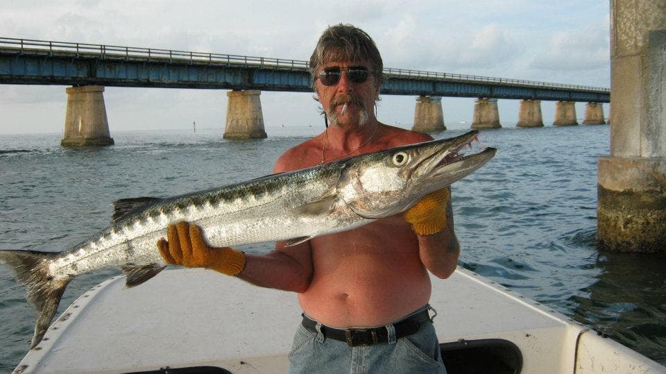 Fisherman holding large barracuda by coastal bridge on boat