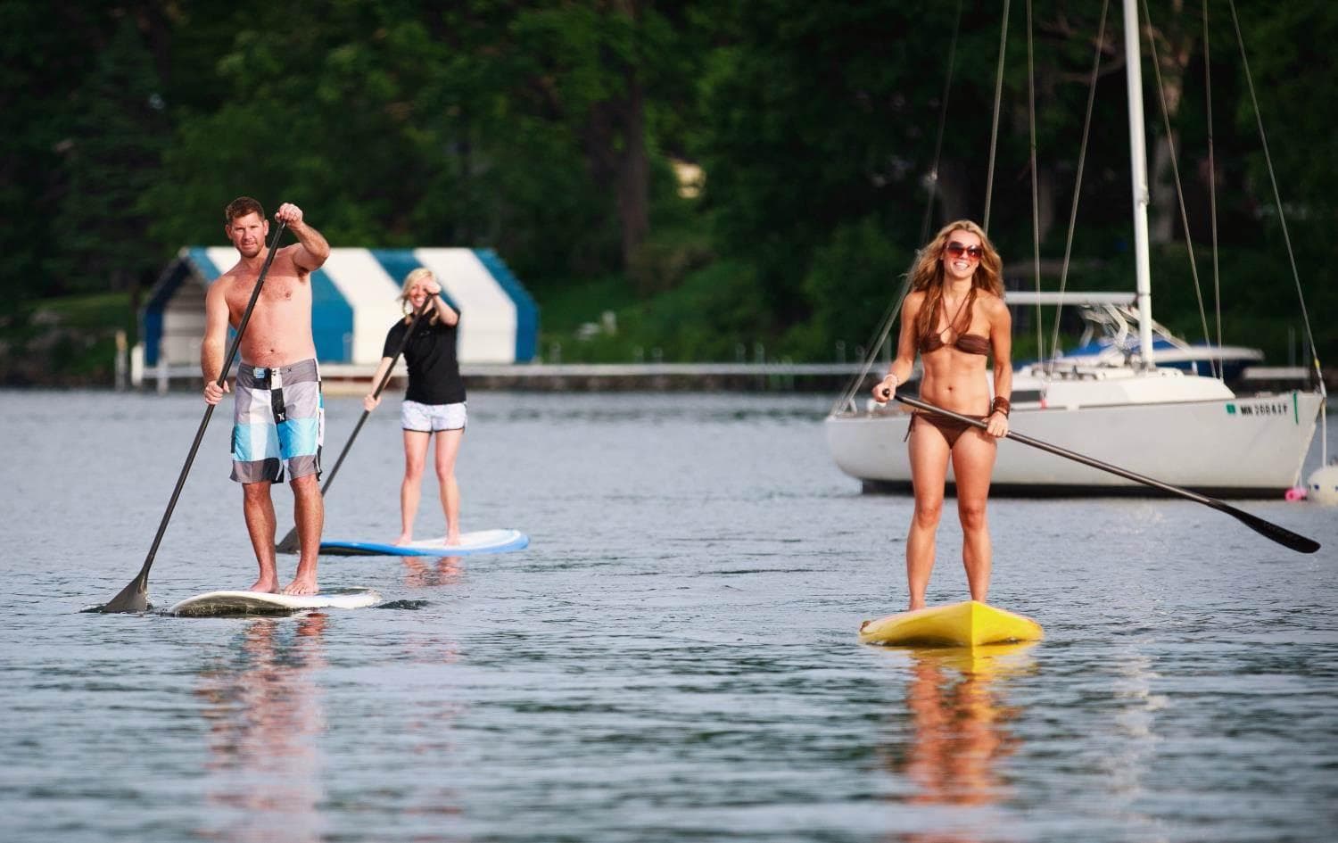 Three people paddleboarding on lake near sailboat