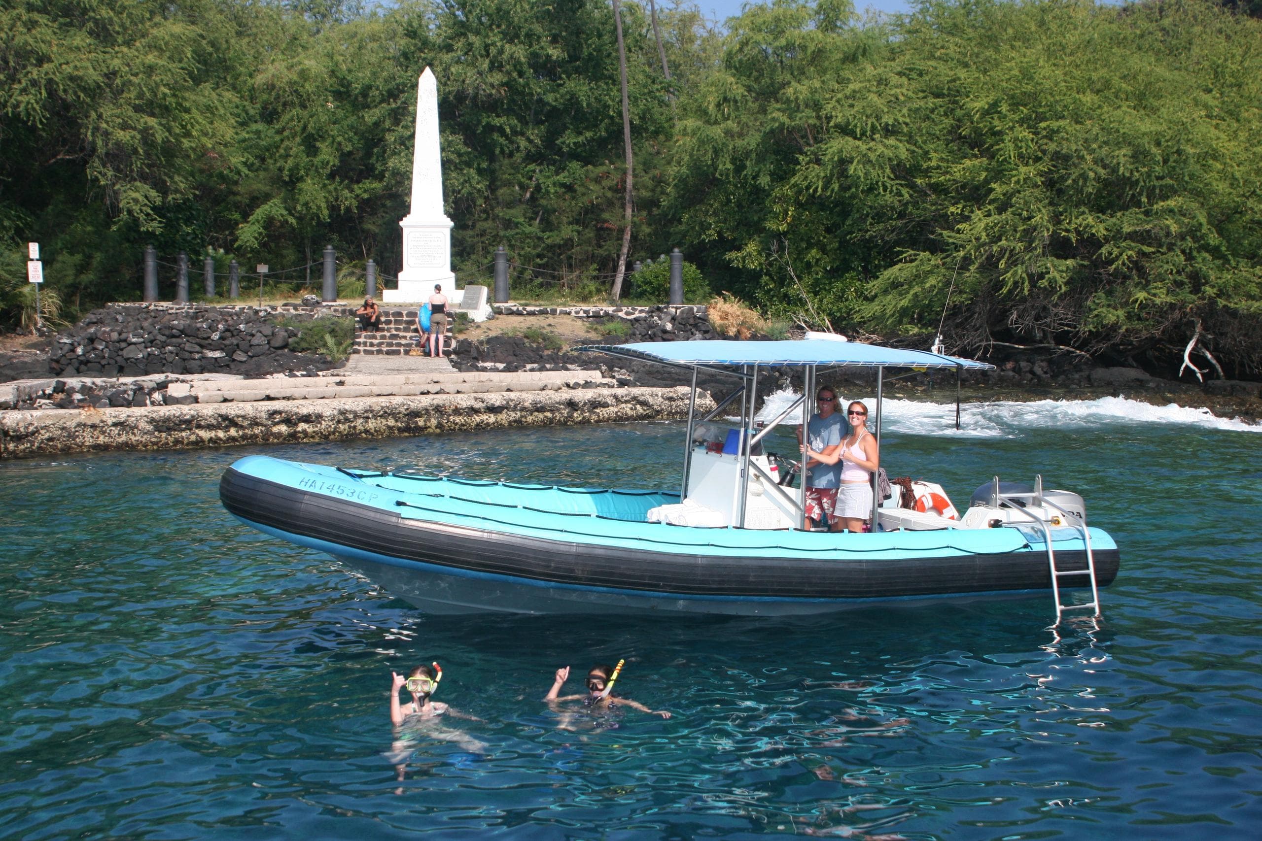 Small sightseeing boat with swimmers near coastal monument