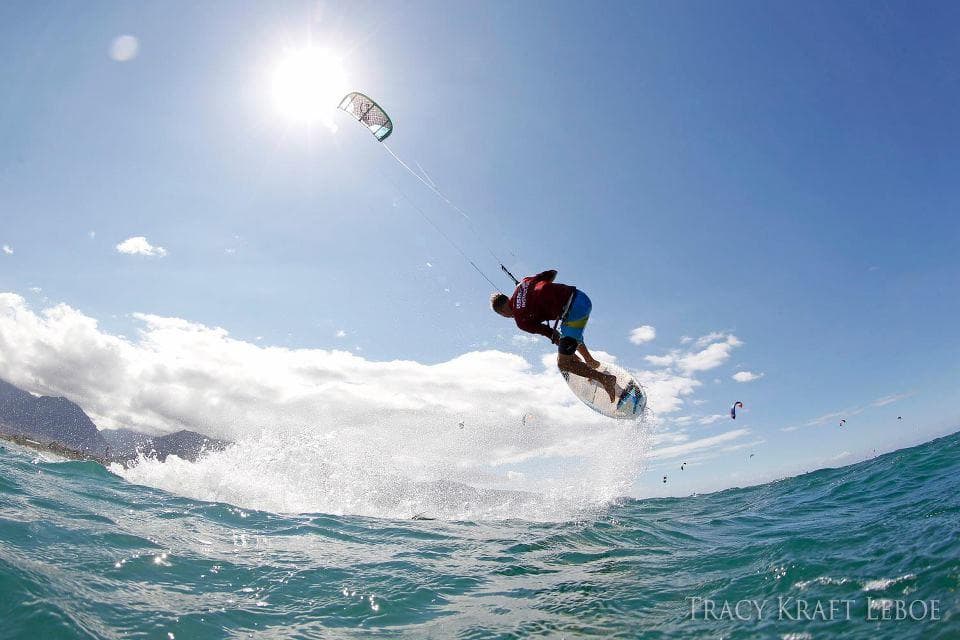 Kiteboarder airborne against sunlit ocean, dramatic jump