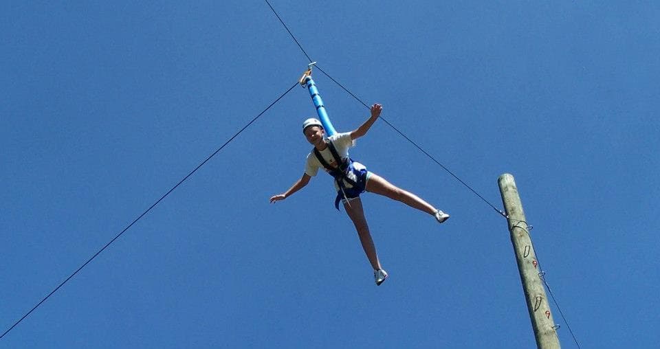 Participant flying on high ropes swing against blue sky