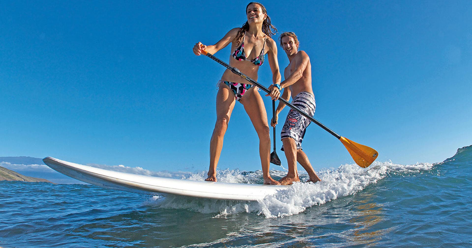 Couple paddleboarding together on calm ocean near shoreline