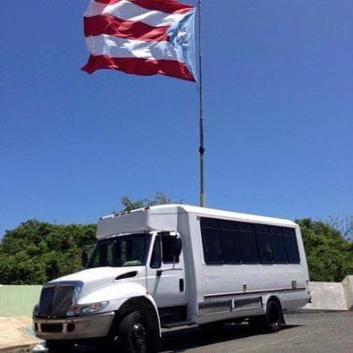 Shuttle bus parked under Puerto Rico flag at sunny port