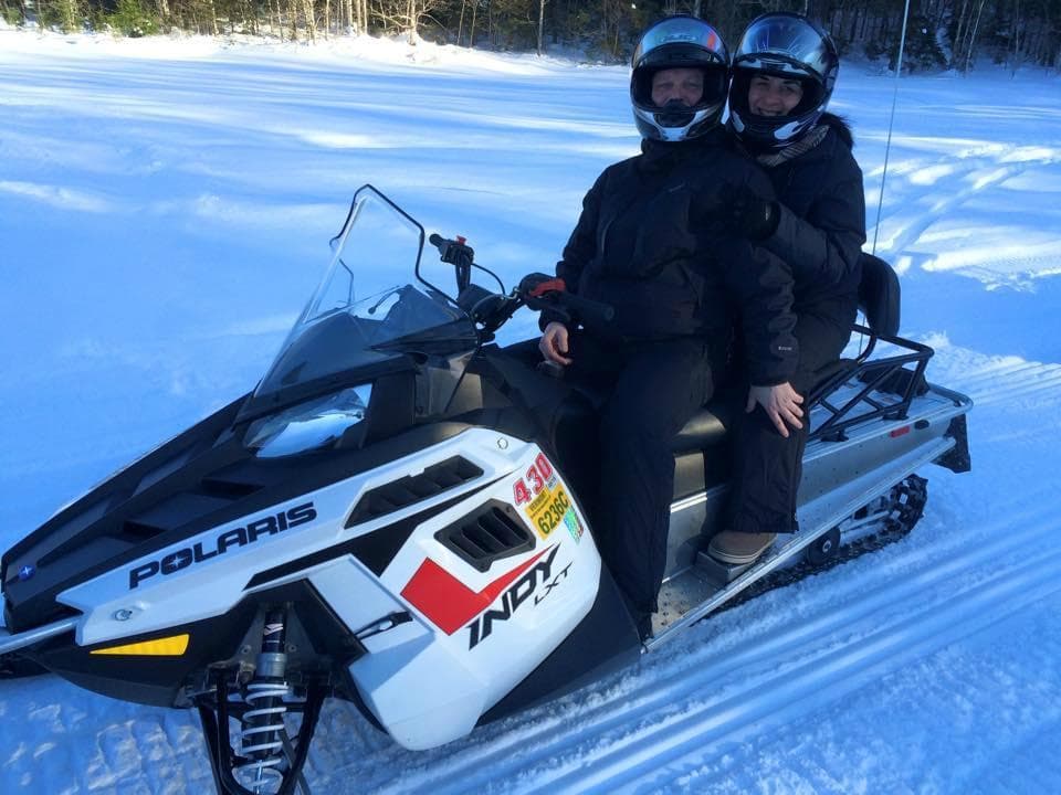 Two riders on tandem snowmobile across groomed snowy trail