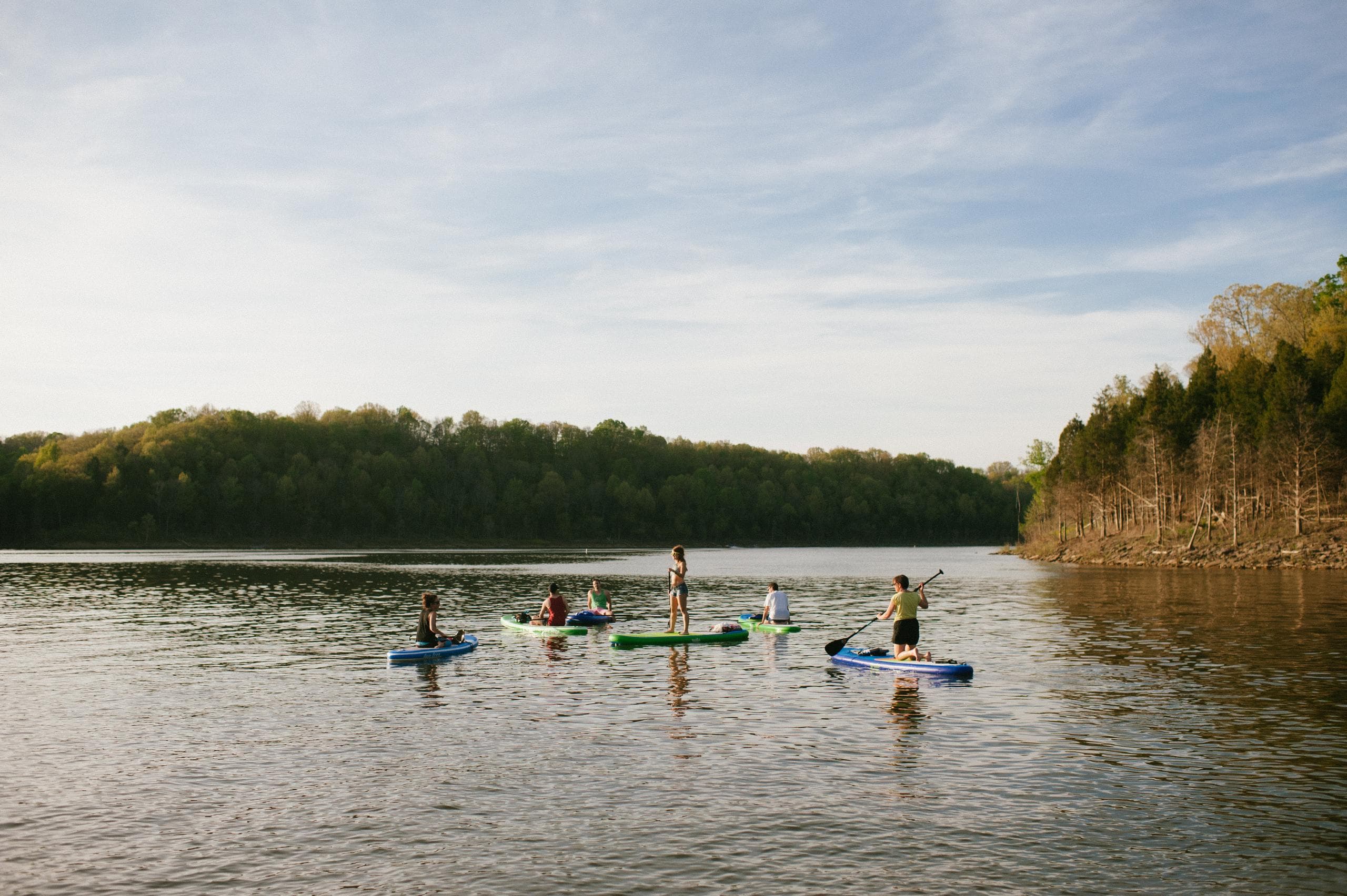 Stand-up paddleboarders on serene forested lake at golden hour