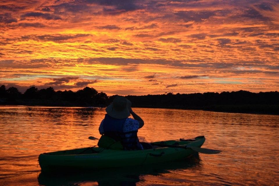 Solo kayaker silhouetted at dramatic coastal sunset marsh