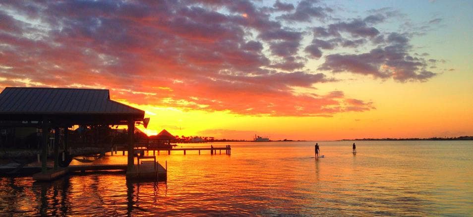 Sunset over coastal pier and calm bay waters, beach skyline