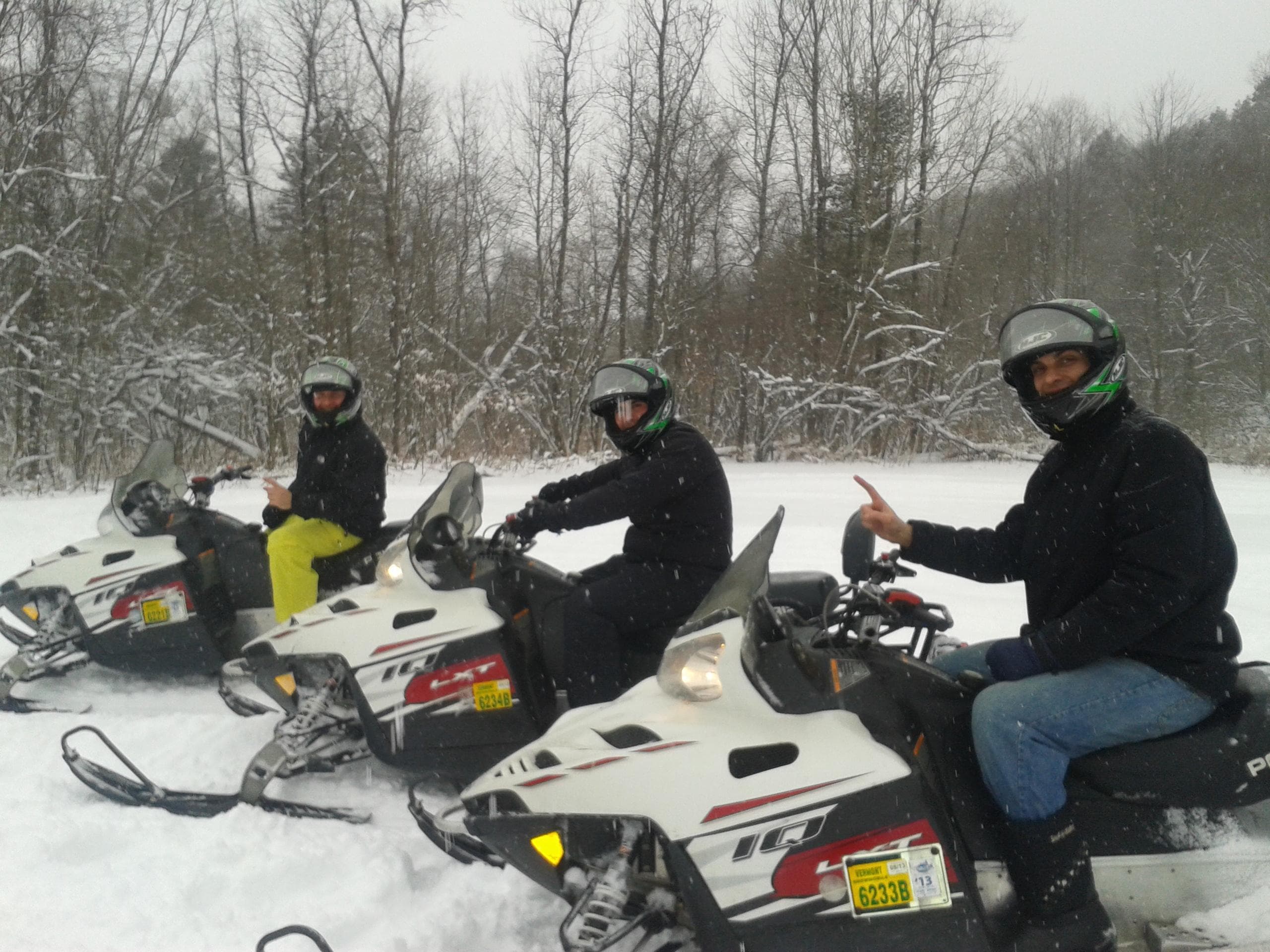 Group of snowmobilers riding through snowy forest trail near trees