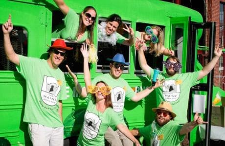 Group of guests cheering by green brewery tour bus outdoors