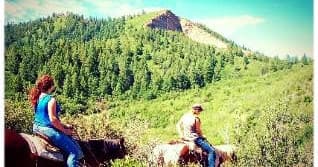 Two riders on trail overlooking forested ridge and valley