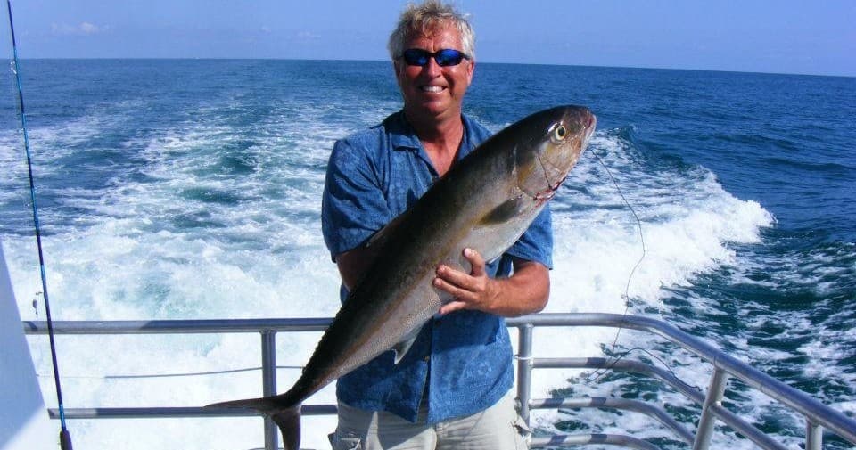 Angler holding big gamefish on stern with ocean wake behind