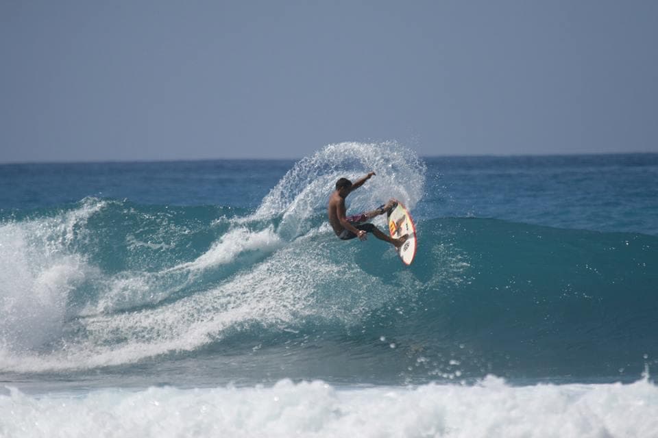 Surfer launching an aerial maneuver over a blue Kona wave