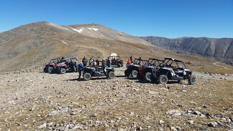 ATVs and UTVs lined on alpine ridge with panoramic mountain views