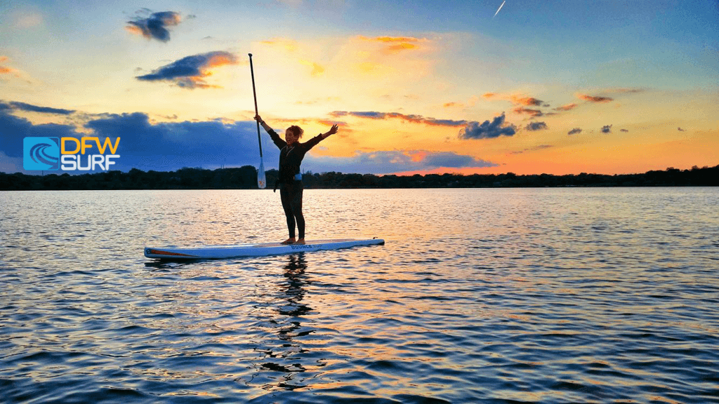 Standup paddler balancing on board at colorful sunset lake