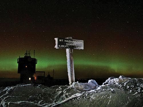 Night aurora and Mount Washington summit sign over icy terrain