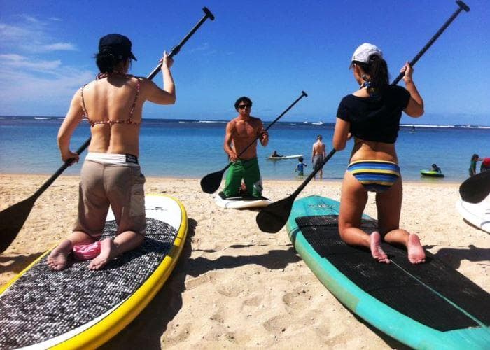 Group standup paddleboarding on sandy beach in Hawaii