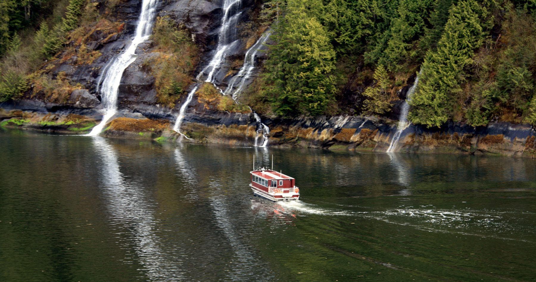 Tour boat cruising past cascading waterfalls in coastal Alaska
