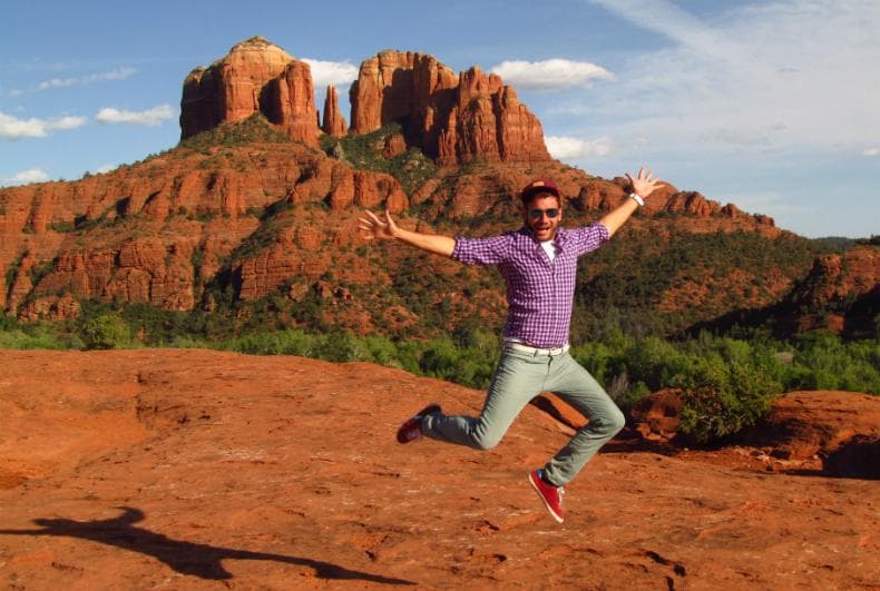 Traveler jumping on red rock trail with Cathedral Rock backdrop