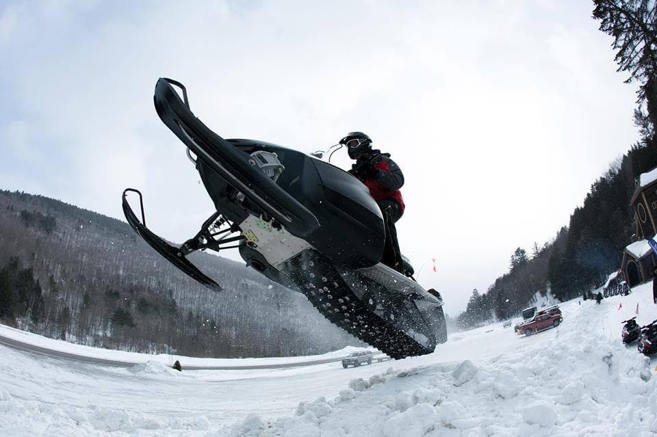 Snowmobile airborne jump over snowy valley in winter mountains