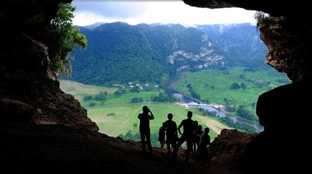 Hikers silhouetted at cave overlook above green valley vista