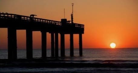Sunset over ocean pier at coastal beach, dramatic sky