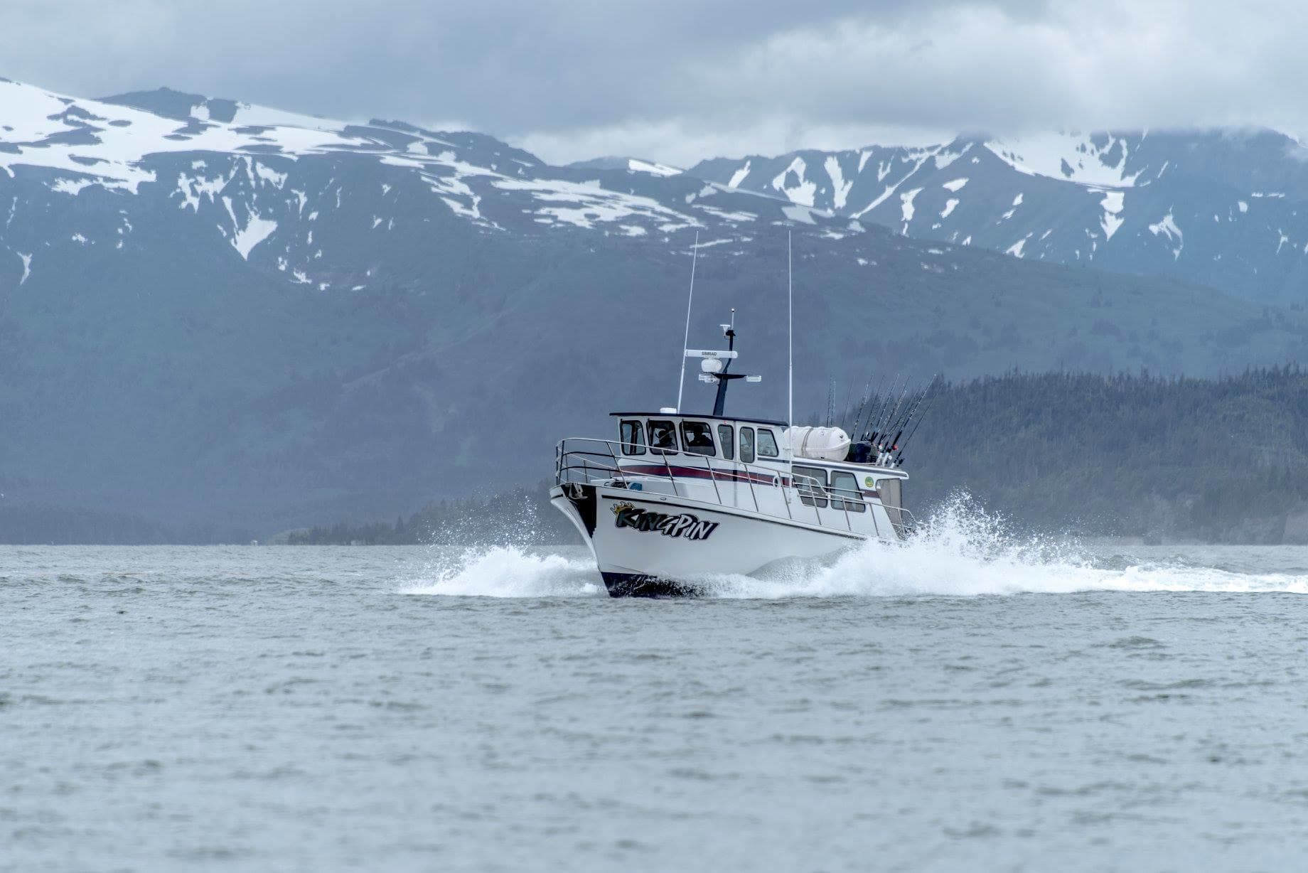 Fishing charter powering through open sea with Alaskan mountains