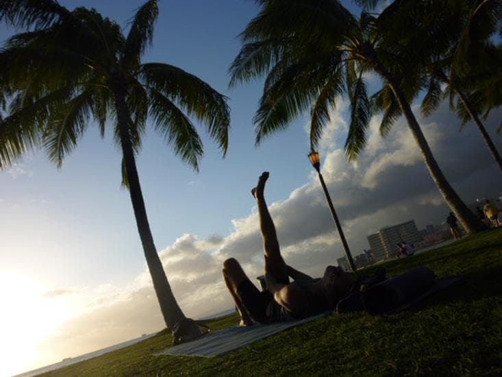 Silhouetted yoga practitioners under palm trees at sunset