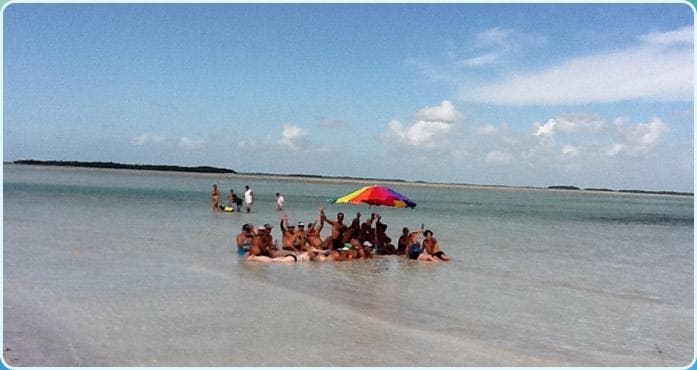Group enjoying shallow sandbar beach with umbrella