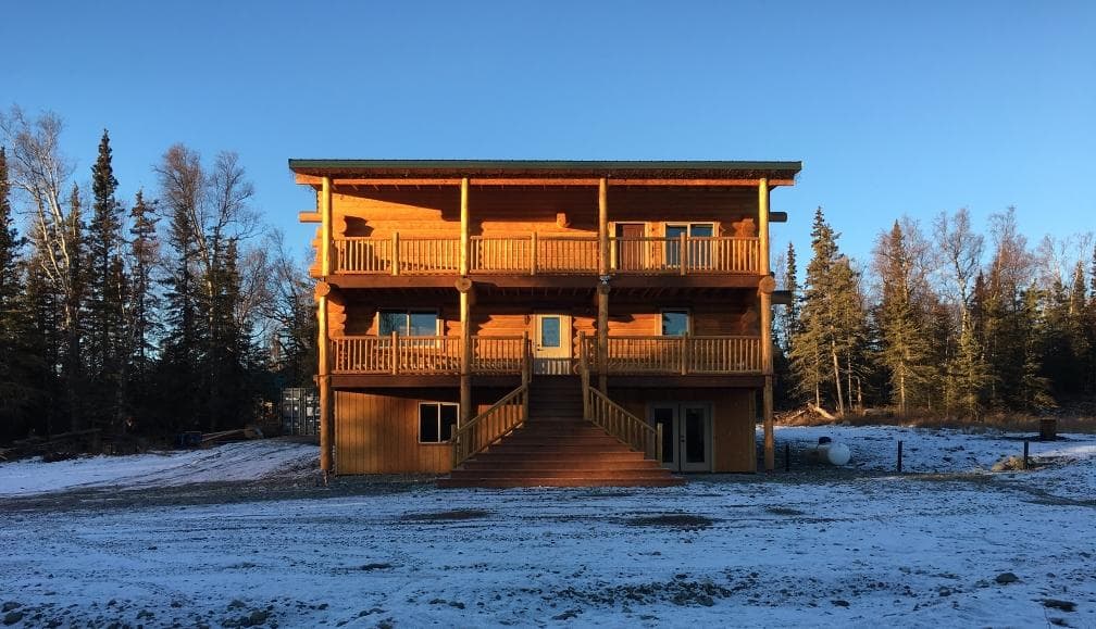Front exterior of rustic Alaska log lodge with snowy grounds and trees