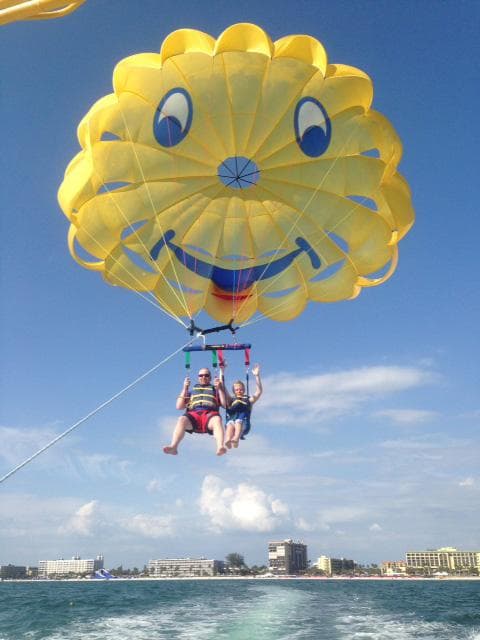 Smiling yellow parasail canopy lifting riders above blue sea