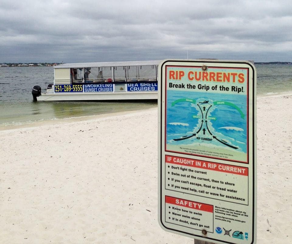 Beach rip current warning sign with tour boat on sandy shore