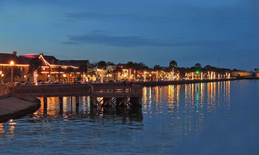 Evening waterfront dining and lit pier reflecting on calm bay