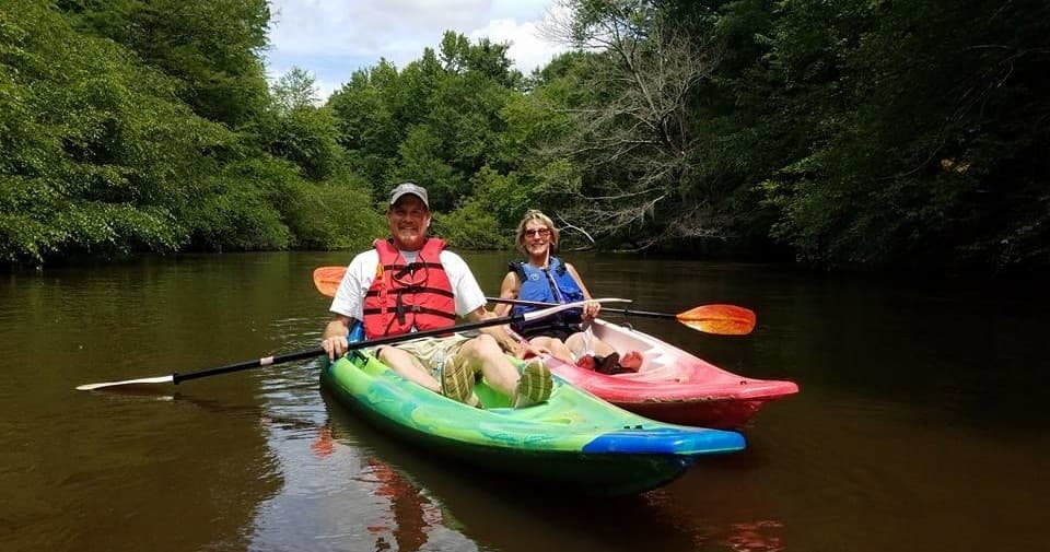 Two kayakers smiling on a tree-lined river, guided paddling tour