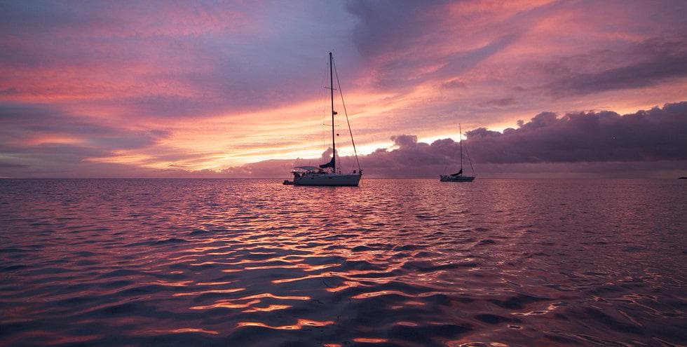 Sailboats silhouetted at vibrant sunset over calm sea