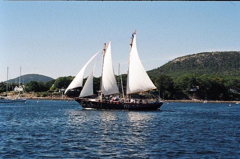 Schooner sailing with white sails along coastal islands