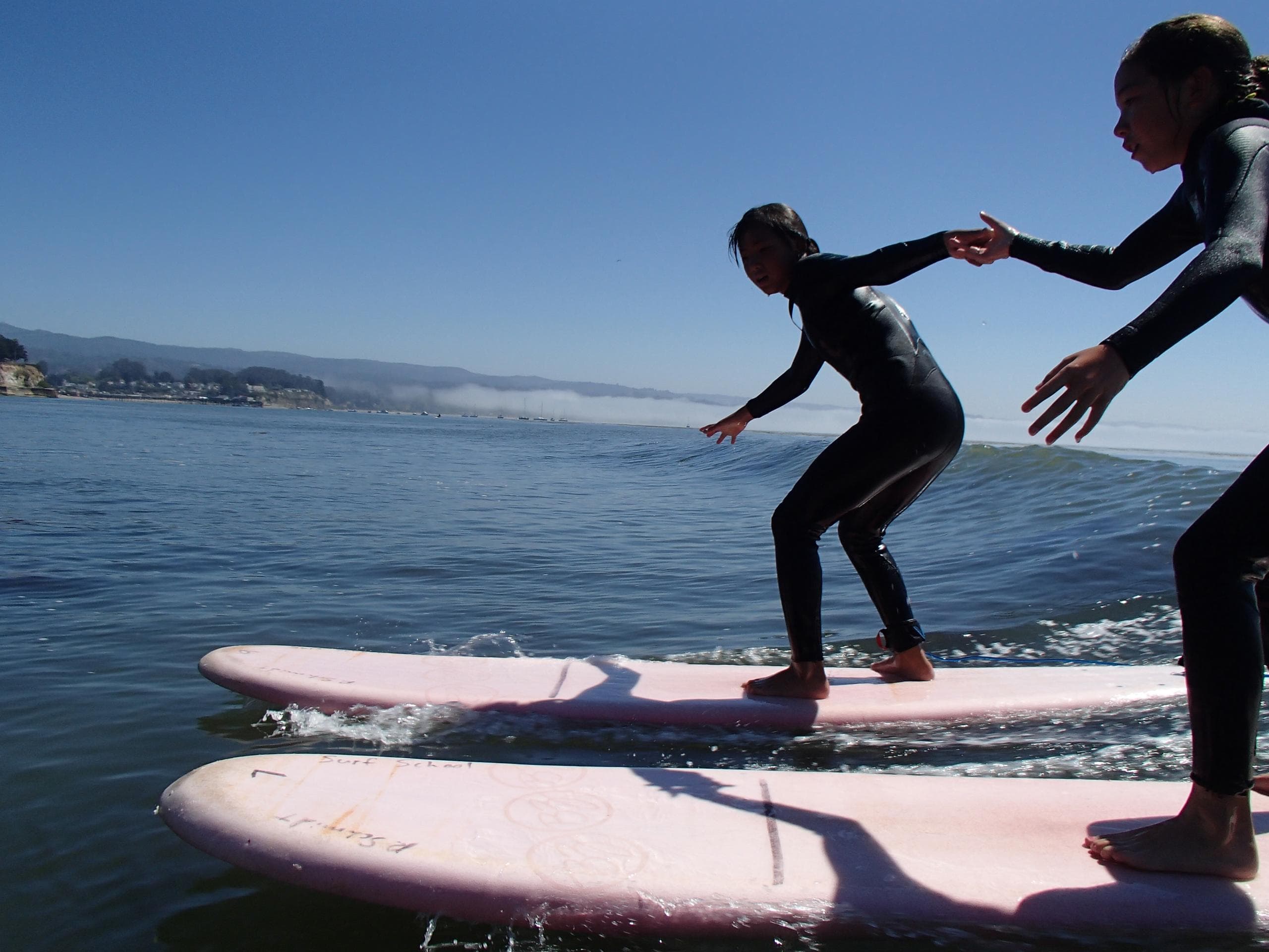 Beginners balancing on longboards in calm bay surf lesson