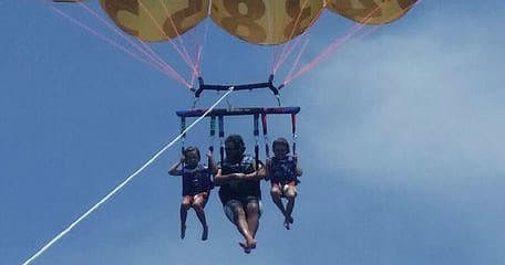 Three-person parasail flight under colorful canopy over open sea