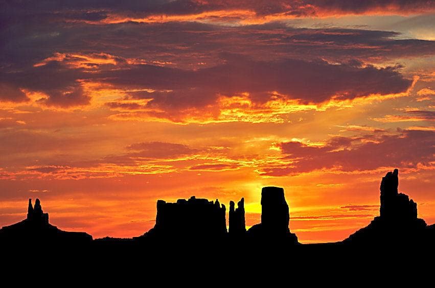 Sunset glow behind Monument Valley spires and silhouettes