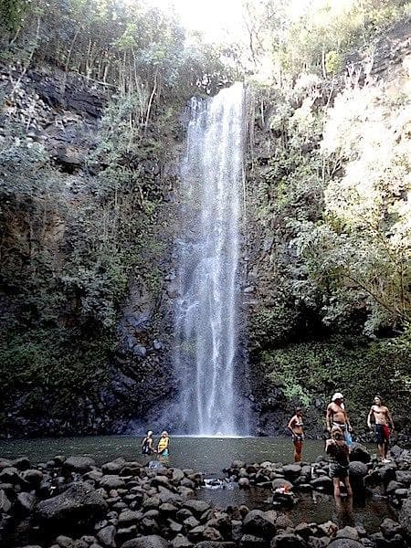 Hikers standing at base of tall jungle waterfall in tropical gorge