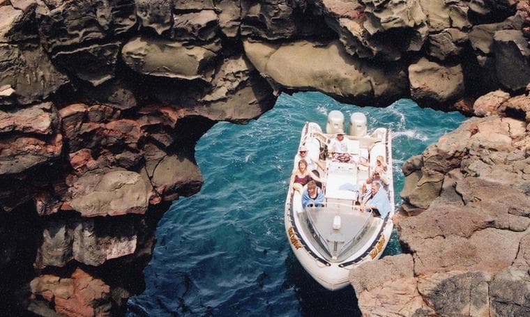 Boat cruising through coastal lava arch, ocean snorkeling tour