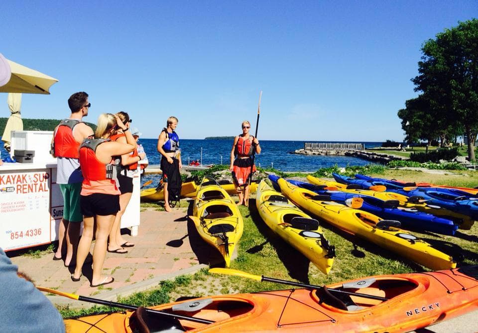 Group preparing kayaks on grassy shore for guided tour