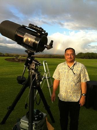 Astronomy guide beside large telescope on Hawaiian lawn at sunset
