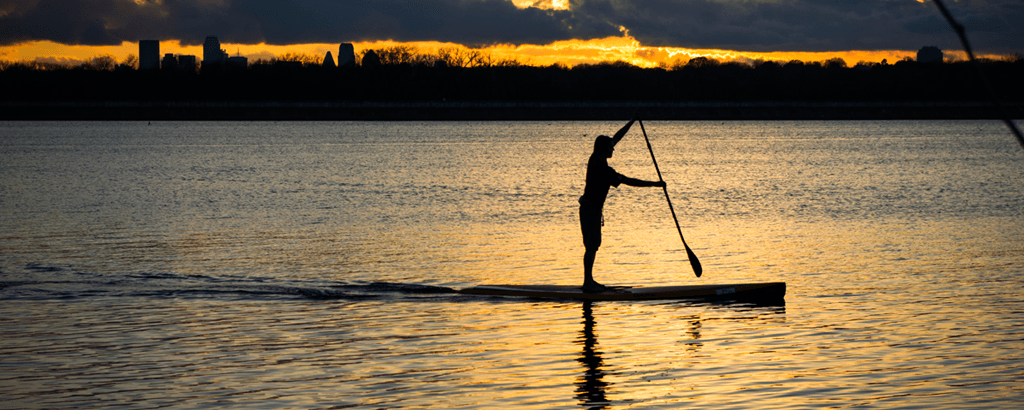 Silhouette paddleboarder gliding across golden sunset waters