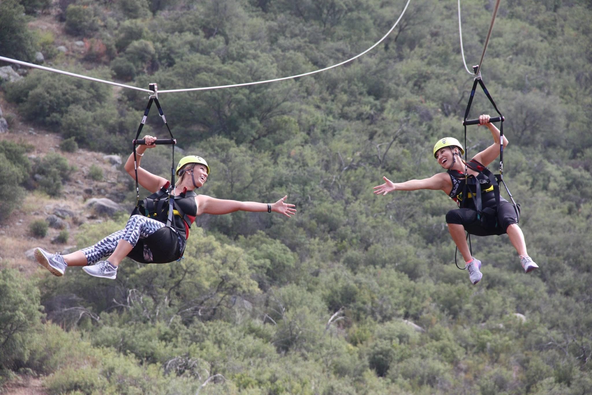Two riders tandem ziplining over scrubby hills with open sky