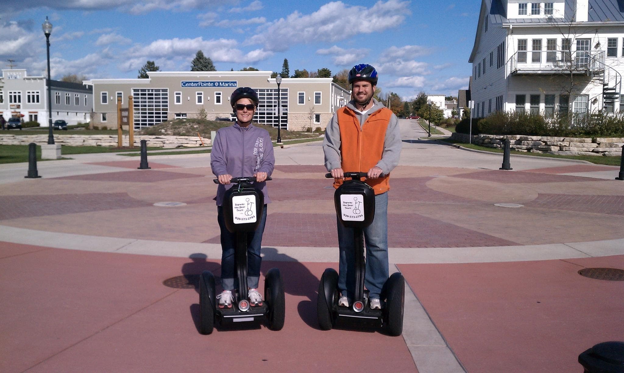 Two riders on Segways in sunny waterfront plaza with historic buildings