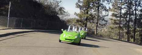 Two riders in bright green scooters cruising scenic coastal road